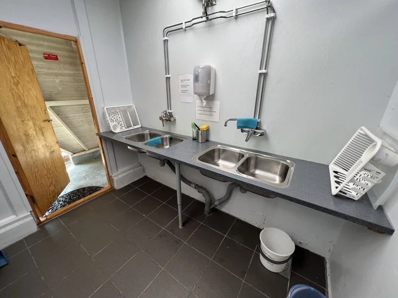 Bilden visar ett kök hos Björkenäs camping, med en diskho utrustad med kökskran och ett kaklat golv.