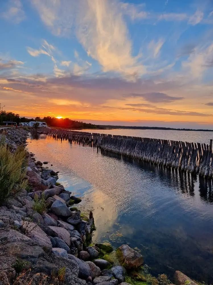 En stämningsfull bild av Böda Hamns Camping visar en vacker horisont med solnedgångens glöd över havet. Den stilla vattenspegeln och den dämpade kvällshimlen skapar en lugn och rofylld atmosfär vid kusten.