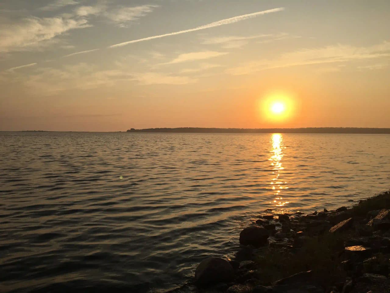 Solnedgång över vatten vid Böda Hamns Camping med horisonten i bakgrunden, varmt ljus sprider sig över himlen och reflekteras i det stilla vattnet.