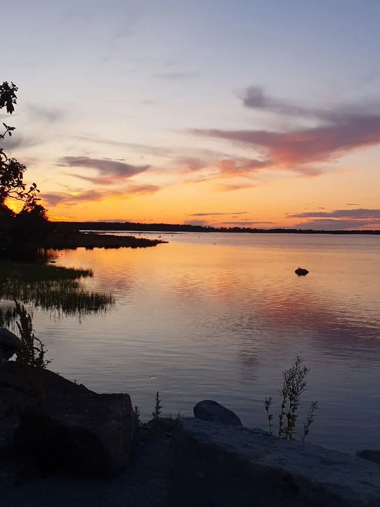 En vacker solnedgång över vattnet vid Böda hamns camping, där himlen glöder i varma färger och speglas på den lugna vattenytan.