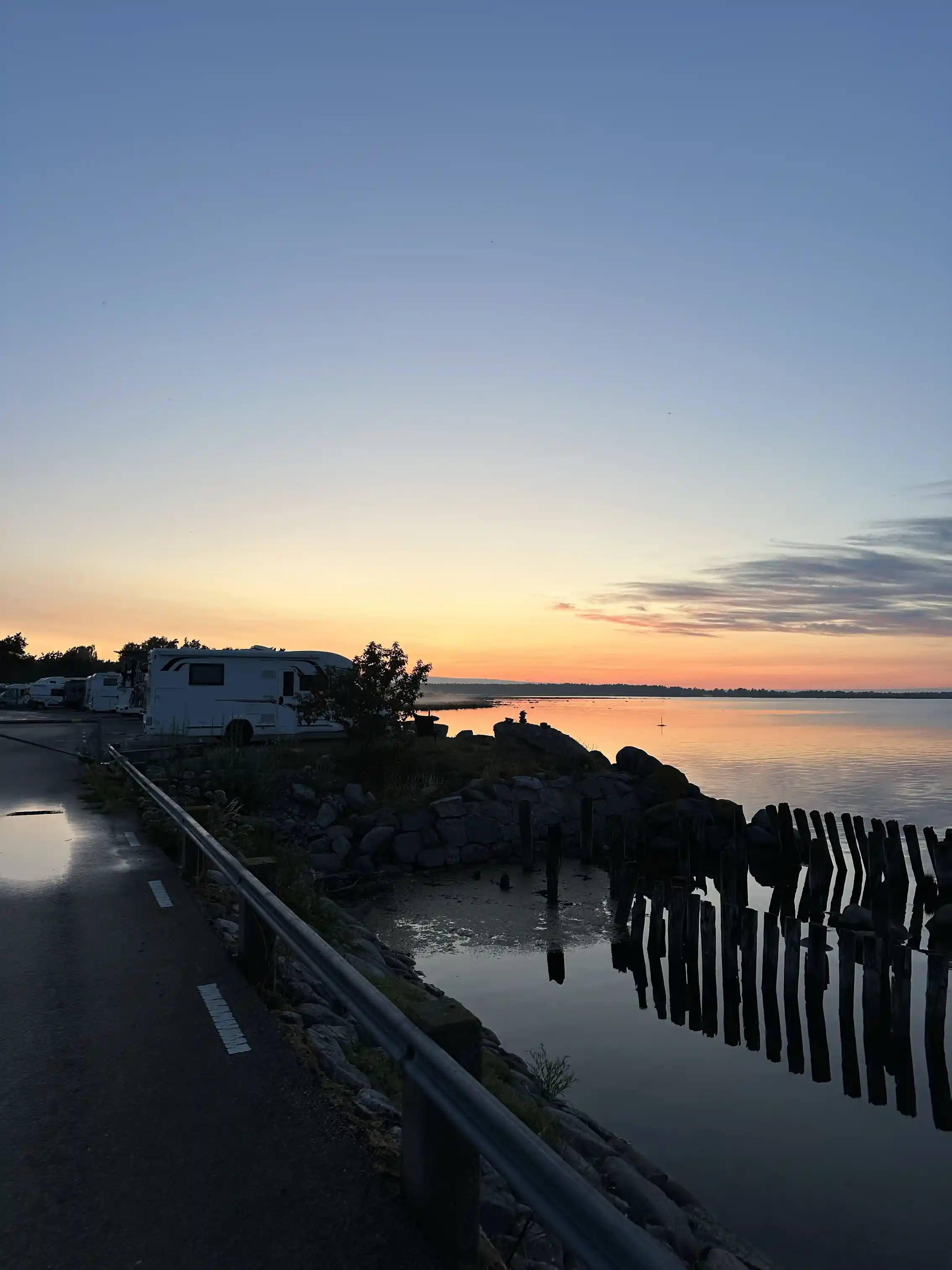 En vacker solnedgång över Böda Hamns Camping, med en klar himmel där solen sakta sänker sig mot horisonten, reflekterande i det lugna vattnet längs kusten.