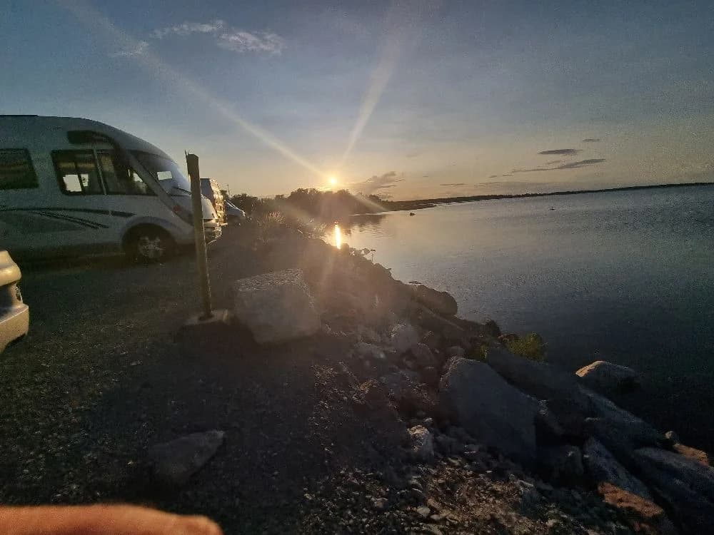 En solnedgång vid Böda Hamns Camping, där solens varma sken reflekteras över kusten och skapar ett stämningsfullt kvällsljus.