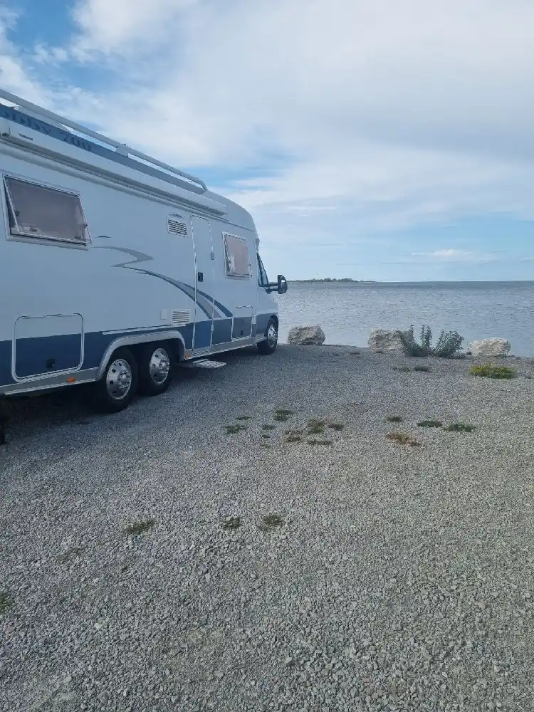En campingplats med flera husbilar och husvagnar parkerade. En semitrailer lastbil syns i bakgrunden. Det är en blåsig dag vid Böda Hamns Camping.
