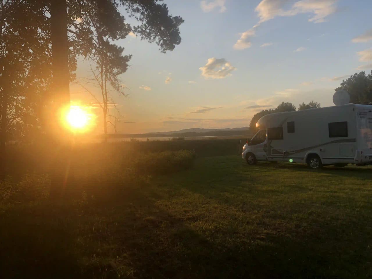 En bild av Storumans camping i solnedgången, med en husvagn i förgrunden och en gyllene himmel i bakgrunden.