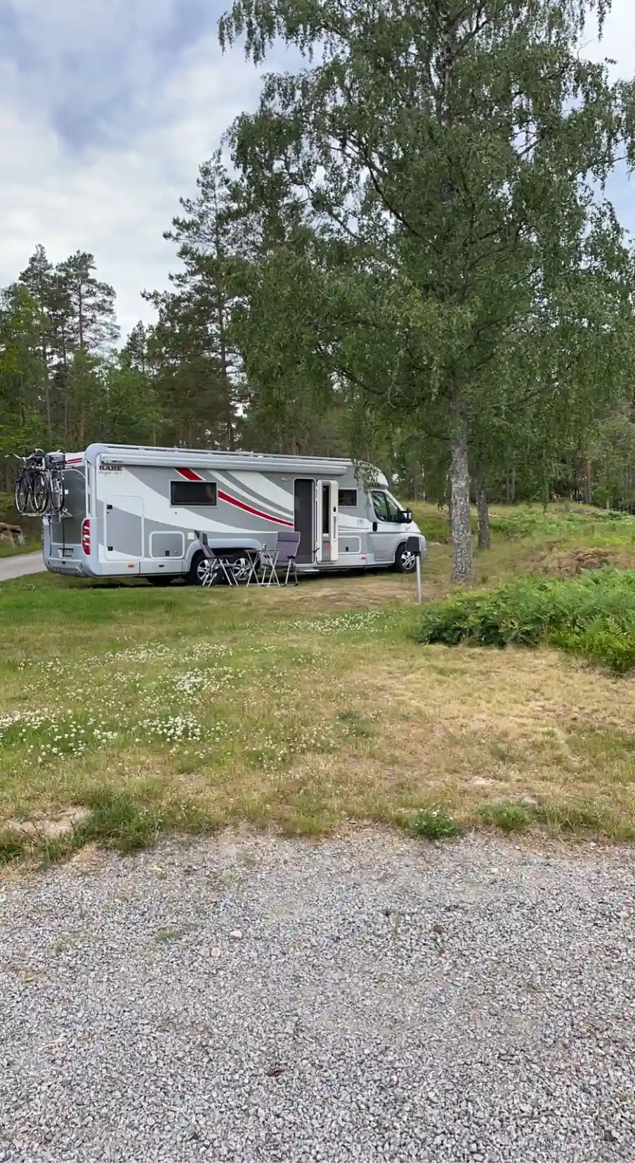 En ställplats i Uvaparken med flera husbilar och lastbilar parkerade på en rymlig yta omgiven av grönskande natur.