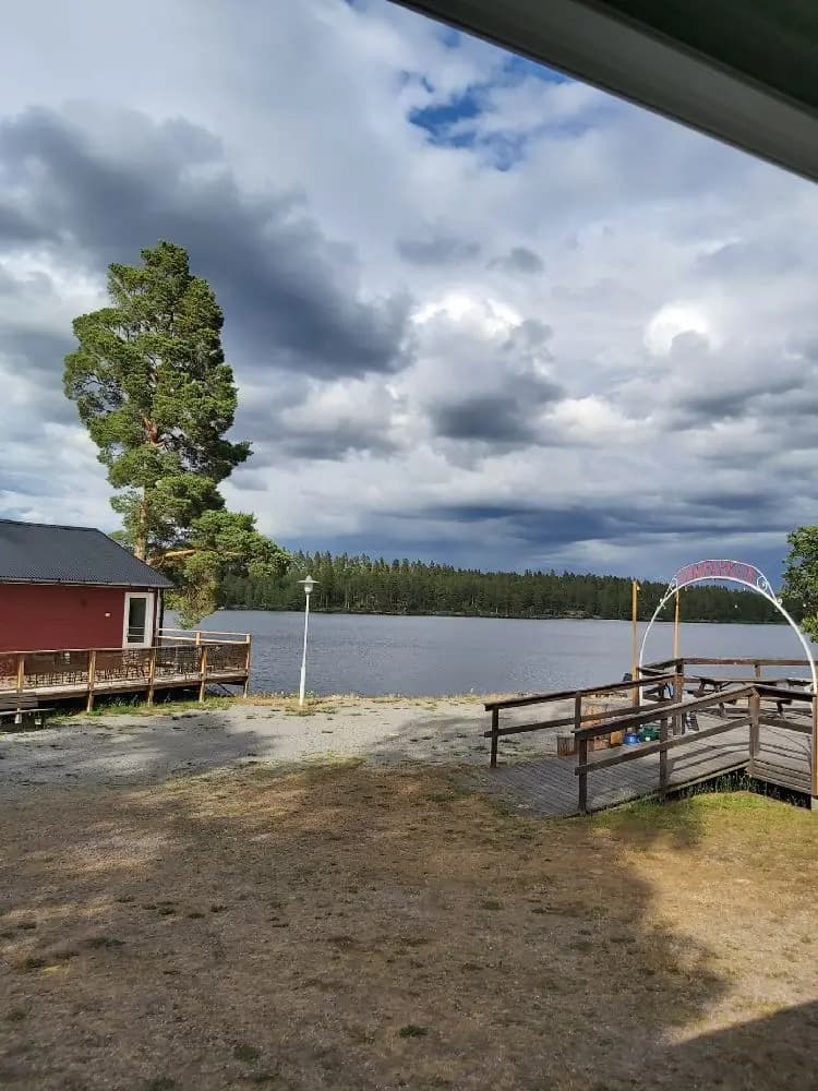 En naturskön vy över en sjö med molntäckt himmel, omgiven av grönskande landskap och en kustlinje. Perfekt för besökare till Uvaparken ställplats.