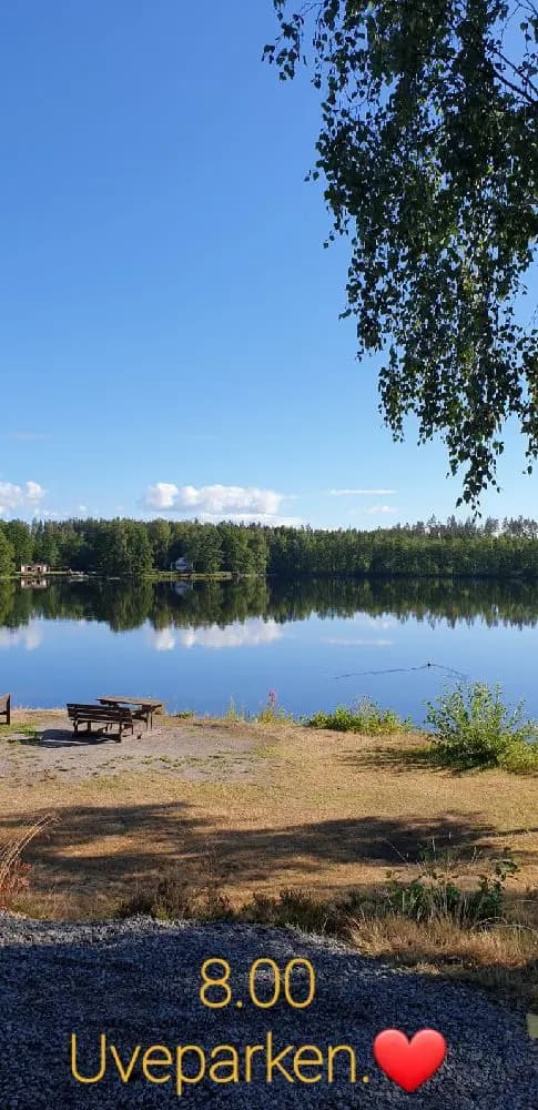 En lugn sjö omgiven av grönskande natur under en klar blå himmel, perfekt för avkoppling och friluftsliv.