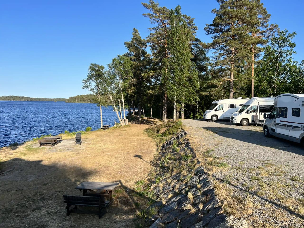 En naturskön vy över en sjö med omgivande kustlandskap vid Uvaparken ställplats, perfekt för en avkopplande paus i naturen.