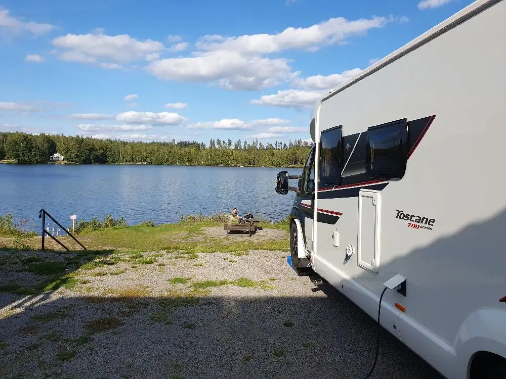 En rad med husbilar och husvagnar parkerade på Uvaparkens ställplats, omgivna av grönska och öppna ytor.