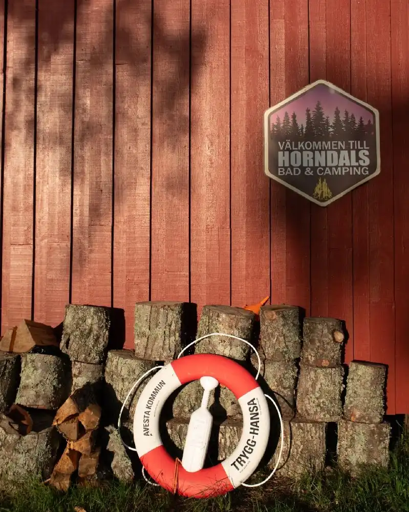 En livboj hänger på en trävägg vid Horndals Bad & Camping, omgiven av plankor av mörkt trä.
