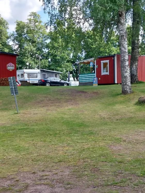 En grönskande campingplats med träd och gräsmatta. En husbil är parkerad i skuggan under träden på Horndals Bad & Camping.