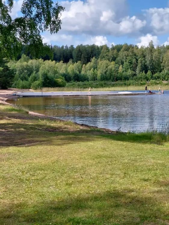 En sommardag vid Horndals bad & camping med frodig växtlighet. En sjö eller flod bredvid en grönskande strand lockar besökare för avkoppling och fritidsaktiviteter.