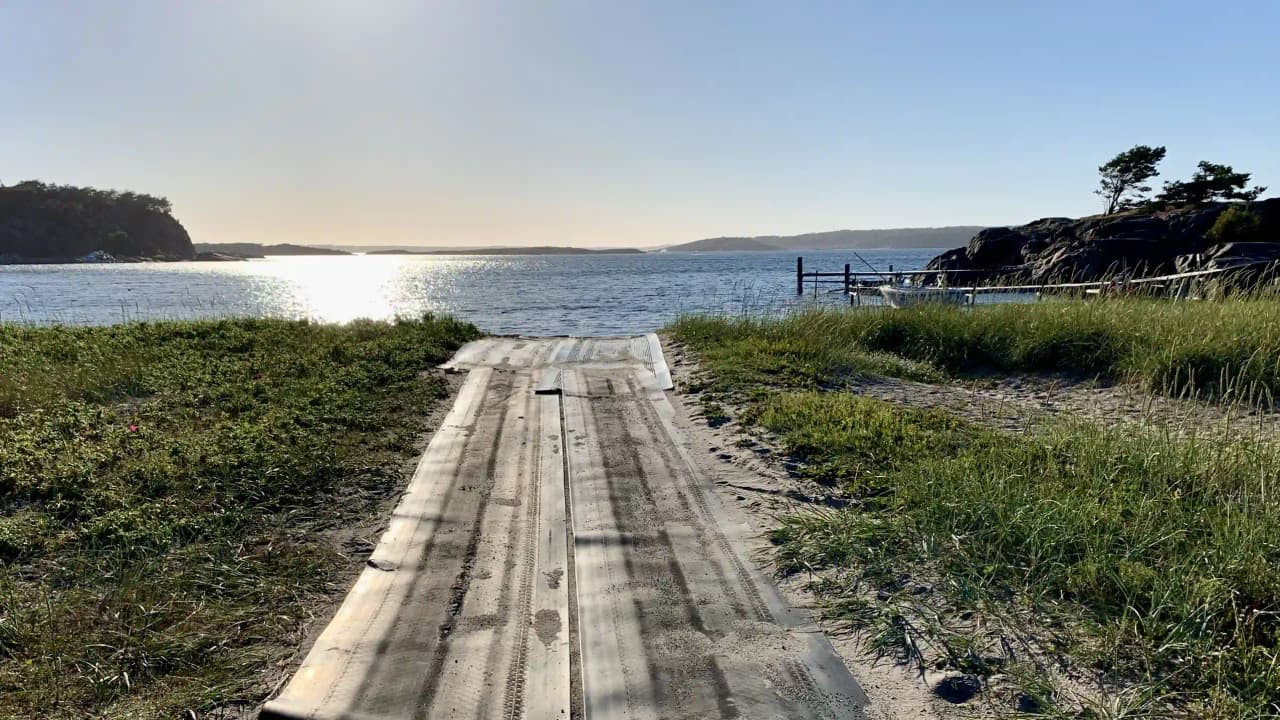 En kustlinje vid Garviks camping med en blandning av vatten och land, som visar en sjö eller hav med en strandpromenad i förgrunden och horisonten synlig i bakgrunden.