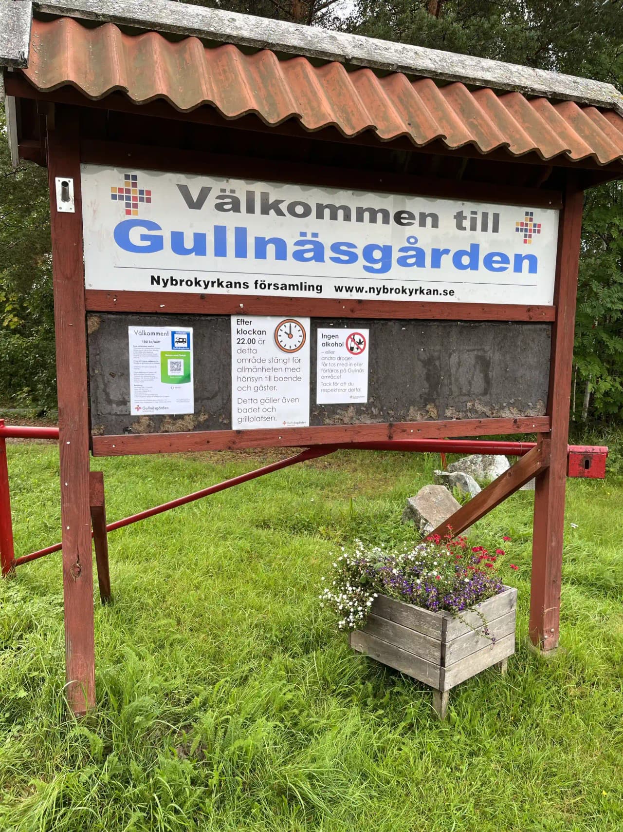 En bild av Gullnäsgården med en skylt och en reklambanner vid en gångstig, omgiven av markvegetation.