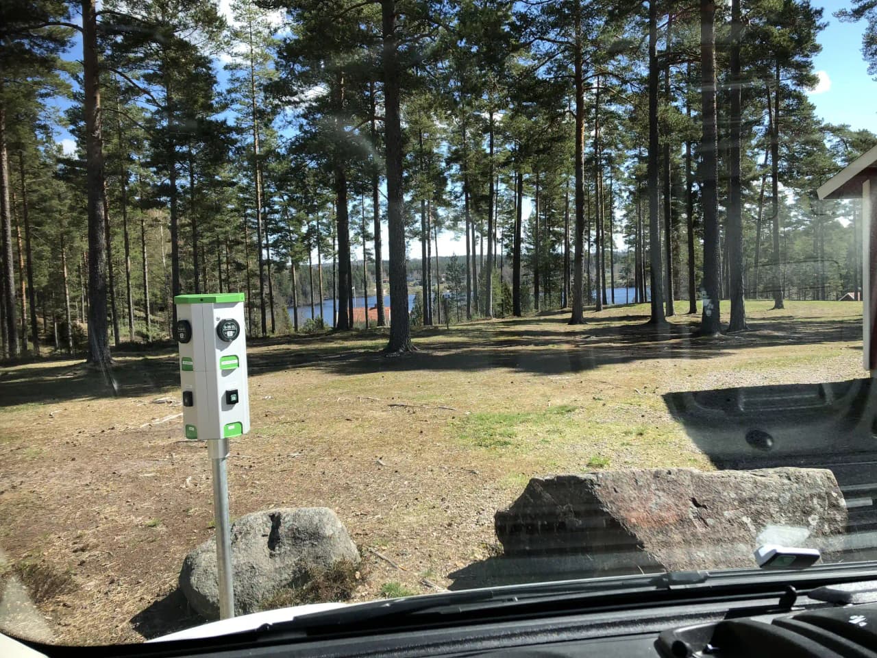 En närbild av en bildörr och ett hjul med navkapsel, mot en bakgrund av en stig i ett naturnära område vid Nyhemsgården.