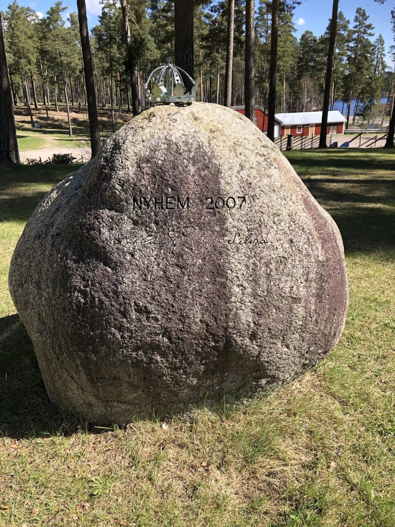 En stor balanserad stenformation på Nyhemsgården, liknande en megalit, omgiven av grönska.