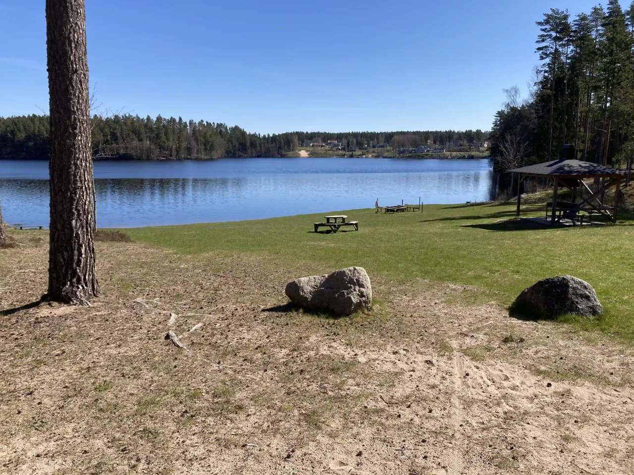 En naturskön vy över en sjö med klart blått vatten, omgiven av grönskande strandkanter och en lugnande atmosfär vid Nyhemsgården.