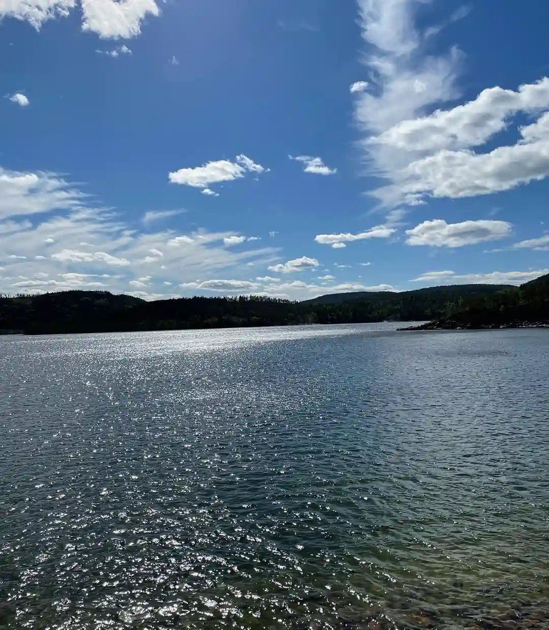 En klarblå himmel speglas i det lugna vattnet vid Måvikens camping & naturområde, där horisonten möter en naturlig och fridfull landskap.