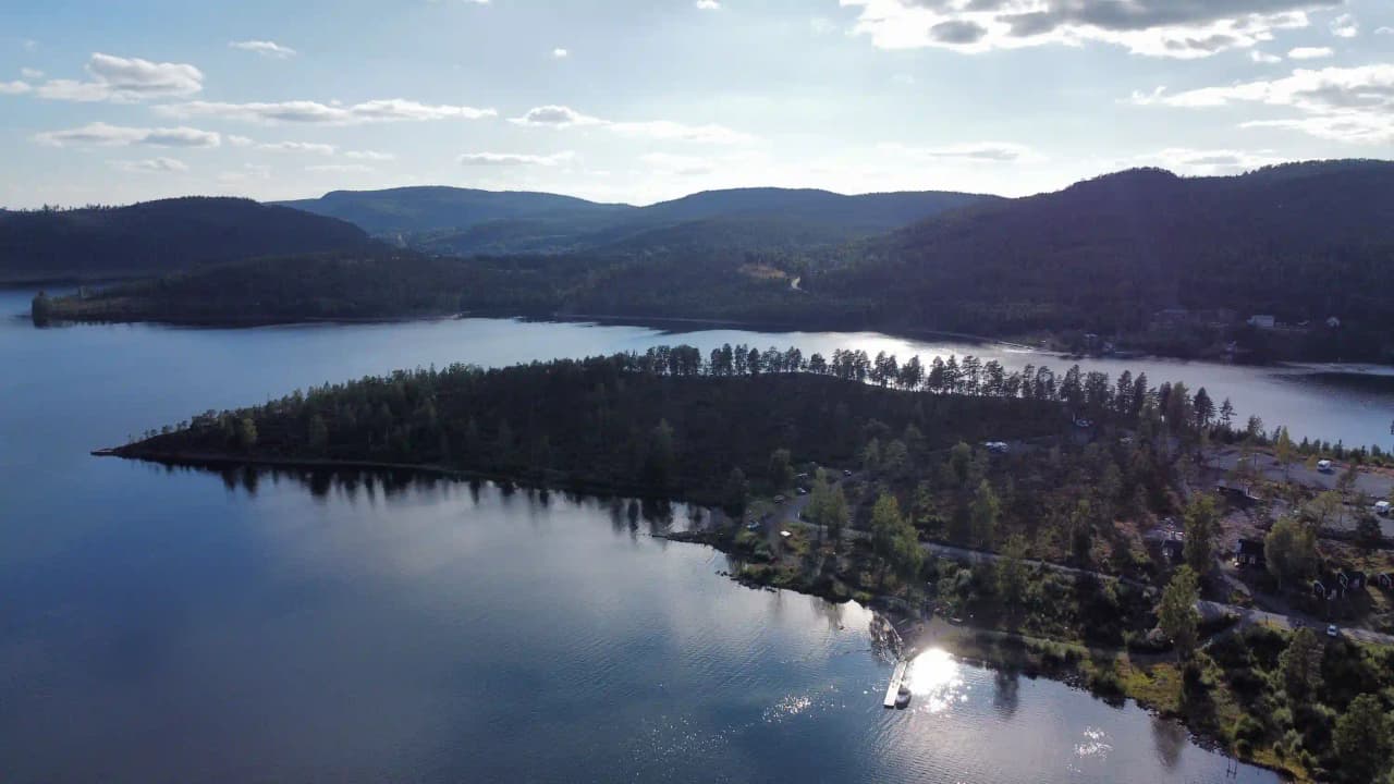 En vidsträckt vy över Måvikens camping & naturområde, med glittrande vatten och omgivande skogslandskap som skapar en rofylld och naturskön miljö.