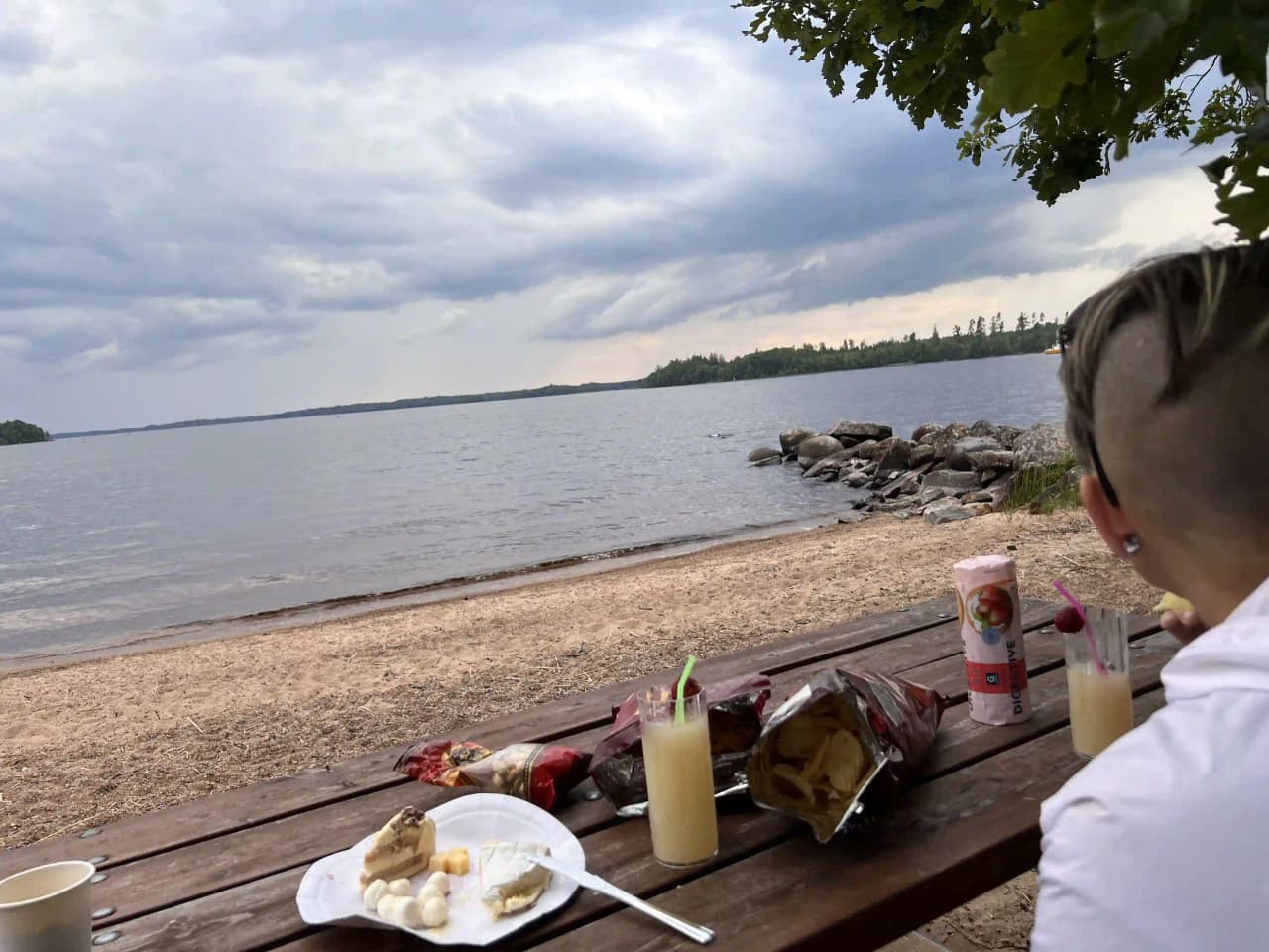 En somrig kustmiljö med vatten i bakgrunden. På stranden finns utemöbler där besökare kan koppla av och njuta av den natursköna omgivningen.