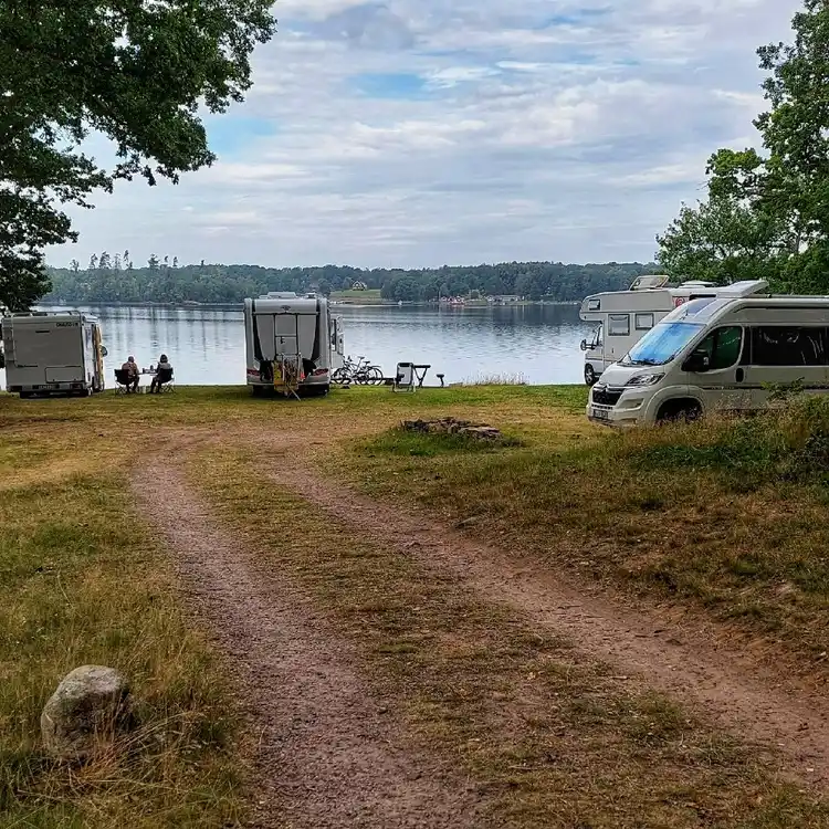 En husvagn och ett tält uppställda på en campingplats i ett naturskönt område vid en sjö.