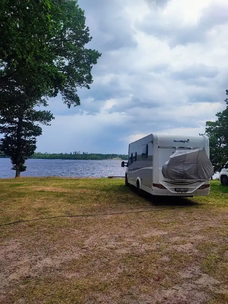 En husbil och en husvagn är parkerade på en grön gräsmatta vid Hägern Bed & Nature. Det är en solig dag och ett träd står i bakgrunden.