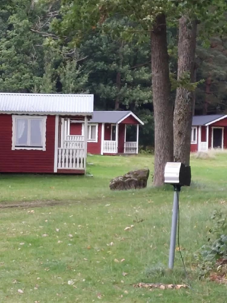 En stuga omgiven av gräsmatta och träd i ett naturskönt område, med små trädgårdsbyggnader i bakgrunden på Hägern Bed & Nature.