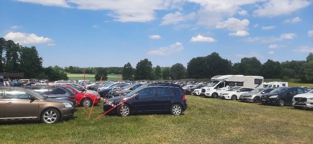 Bild av en parkerad bil på en parkeringsplats vid Kvarngården Hembygdsgård. I bakgrunden syns delar av gårdens omgivning.