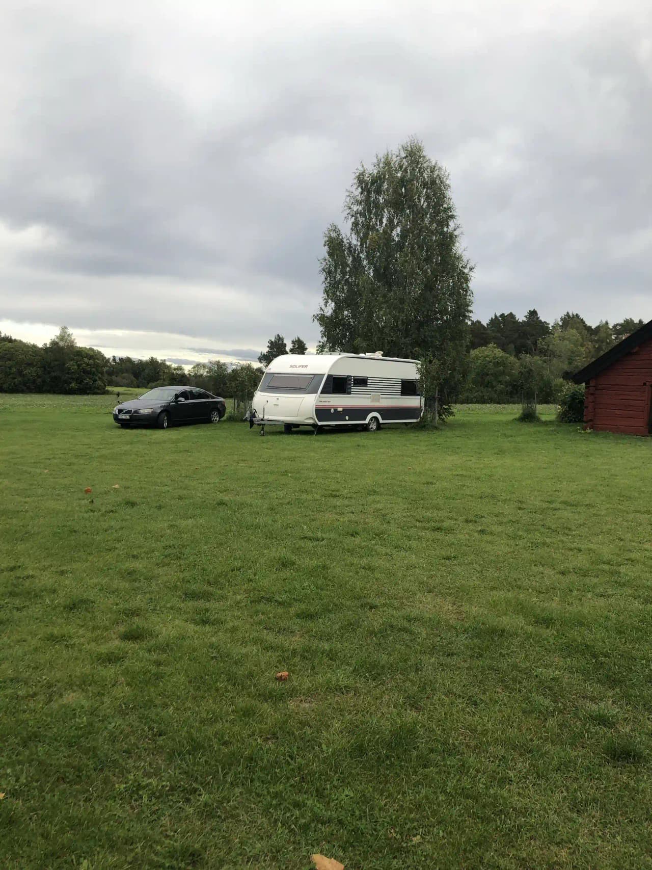 En lyxig husbil parkerad på en grön gräsmatta vid Kvarngården Hembygdsgård, omgiven av öppna fält och under en molnig himmel.