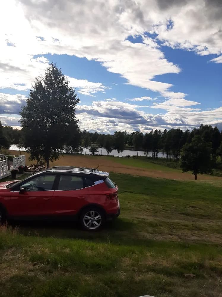 En bil står parkerad framför en molnig himmel vid Påarps gård. Det är en kompakt SUV med synliga bakljus, omgiven av öppet landskap.