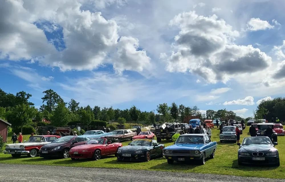 En klassisk bil parkerad vid Tykarpsgrottans camping, omgiven av grönska och andra bilar.