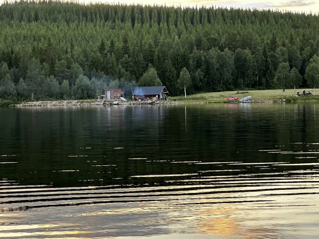En bild av en stillsam sjö med flera båtar flytande på vattnet. Sjön omges av frodiga, gröna stränder, vilket skapar en lugn och inbjudande atmosfär.