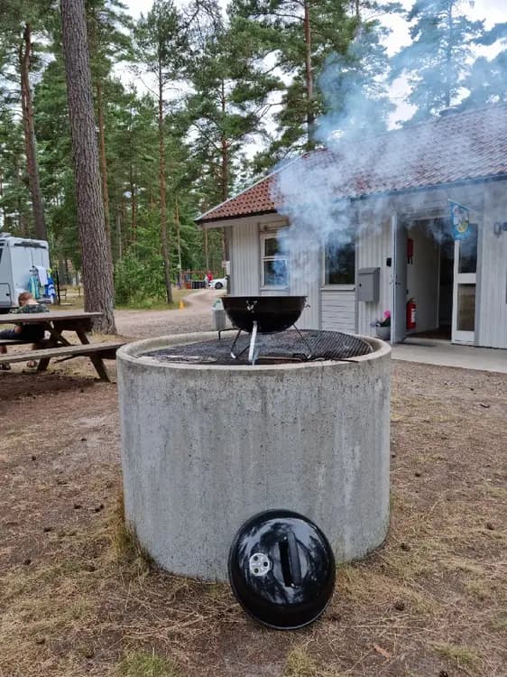 En grönskande bakgård vid Åhus missionsgård, omgiven av stora träd och välklippta buskar, med ett område för avkoppling och samvaro i centrum av bilden.