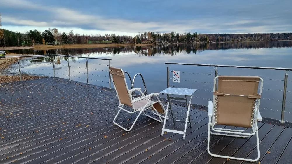 Utomhusmöbelgrupp på trädäck vid en sjö, med stolar och bord av trä.