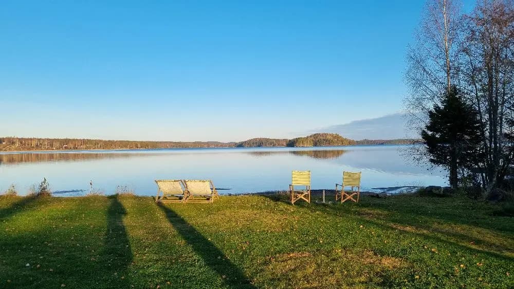 Vy över en fridfull sjö omgiven av grönska, med blå himmel och morgondis i fjärran.