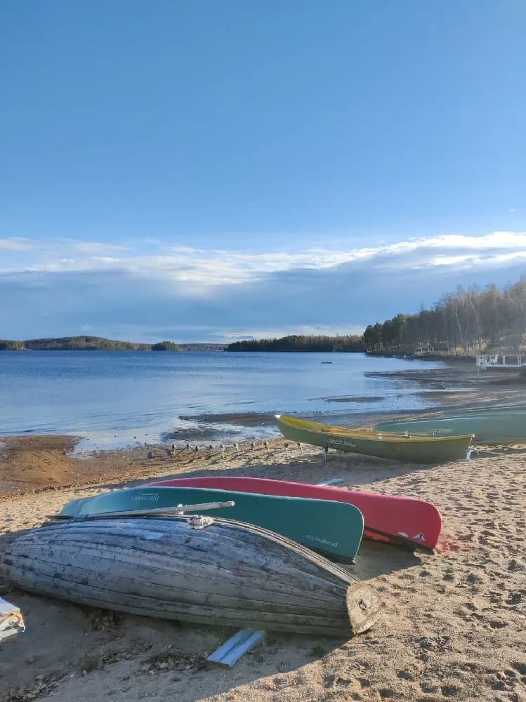 Bild av en liten båt förtöjd vid en sandstrand invid kustlinjen, omgiven av ett lugnt hav och en småstensstrand på Sagaliden.