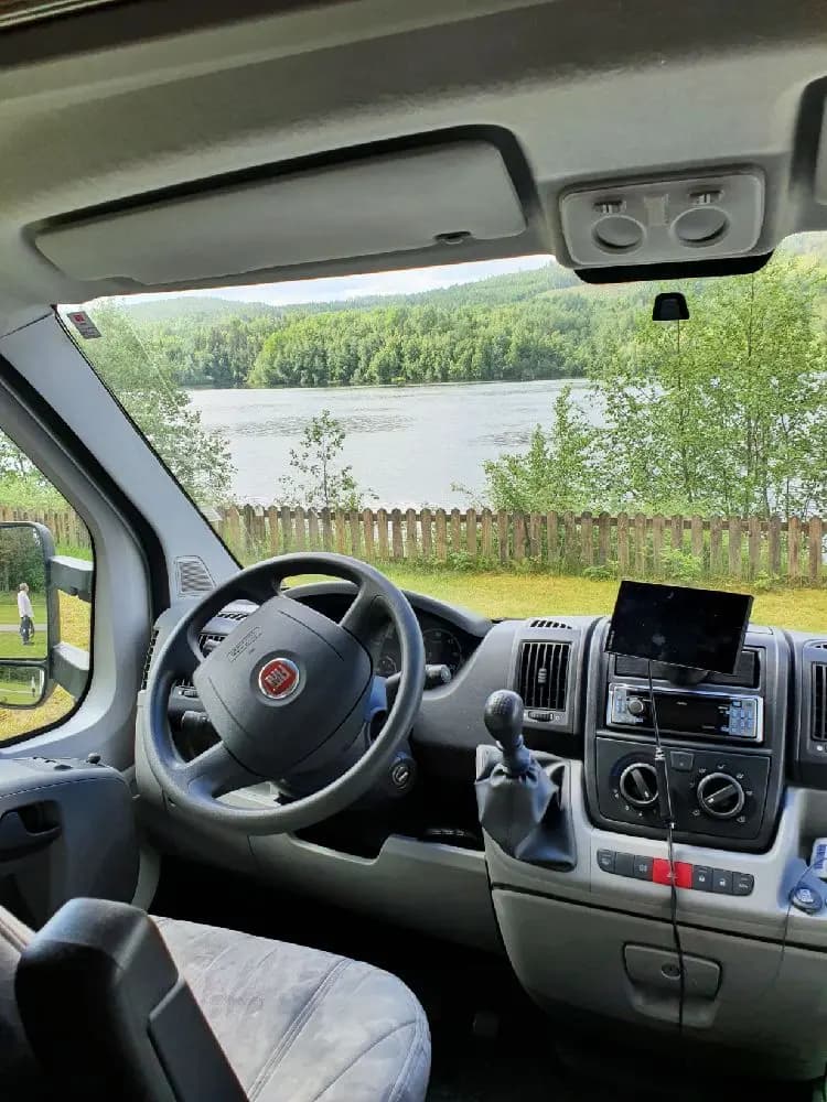 En minivan står parkerad vid Kävsta camping, omgiven av grönska. Den speglar den praktiska sidan av campinglivet med lätt tillgång till transport och bekvämligheter.