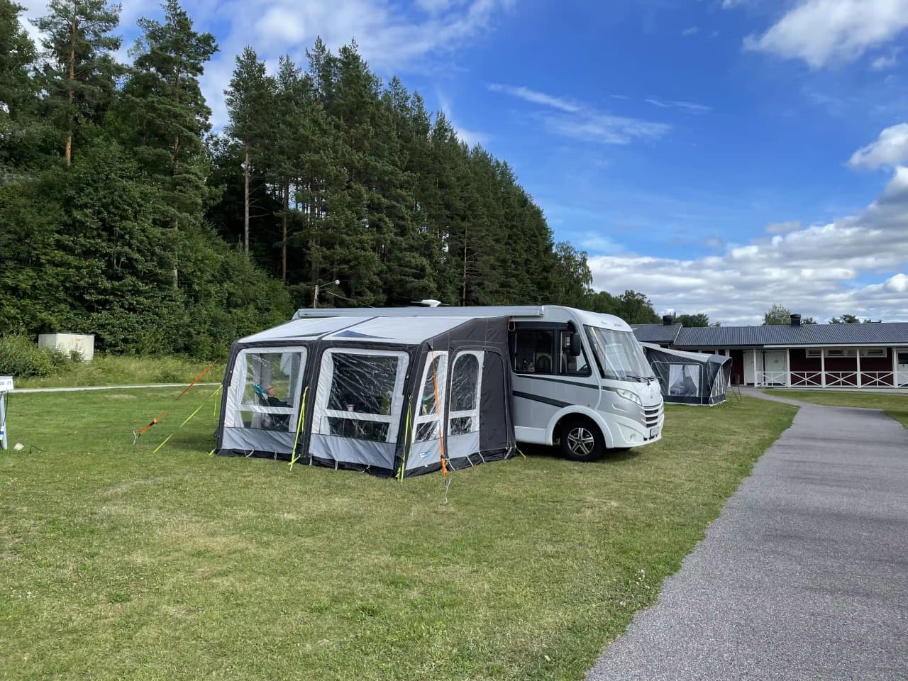 En husbil står parkerad vid Kävsta camping, med utfälld markis för att skapa skugga. Bredvid syns en minivan med öppna dörrar, omgiven av grönskande natur.