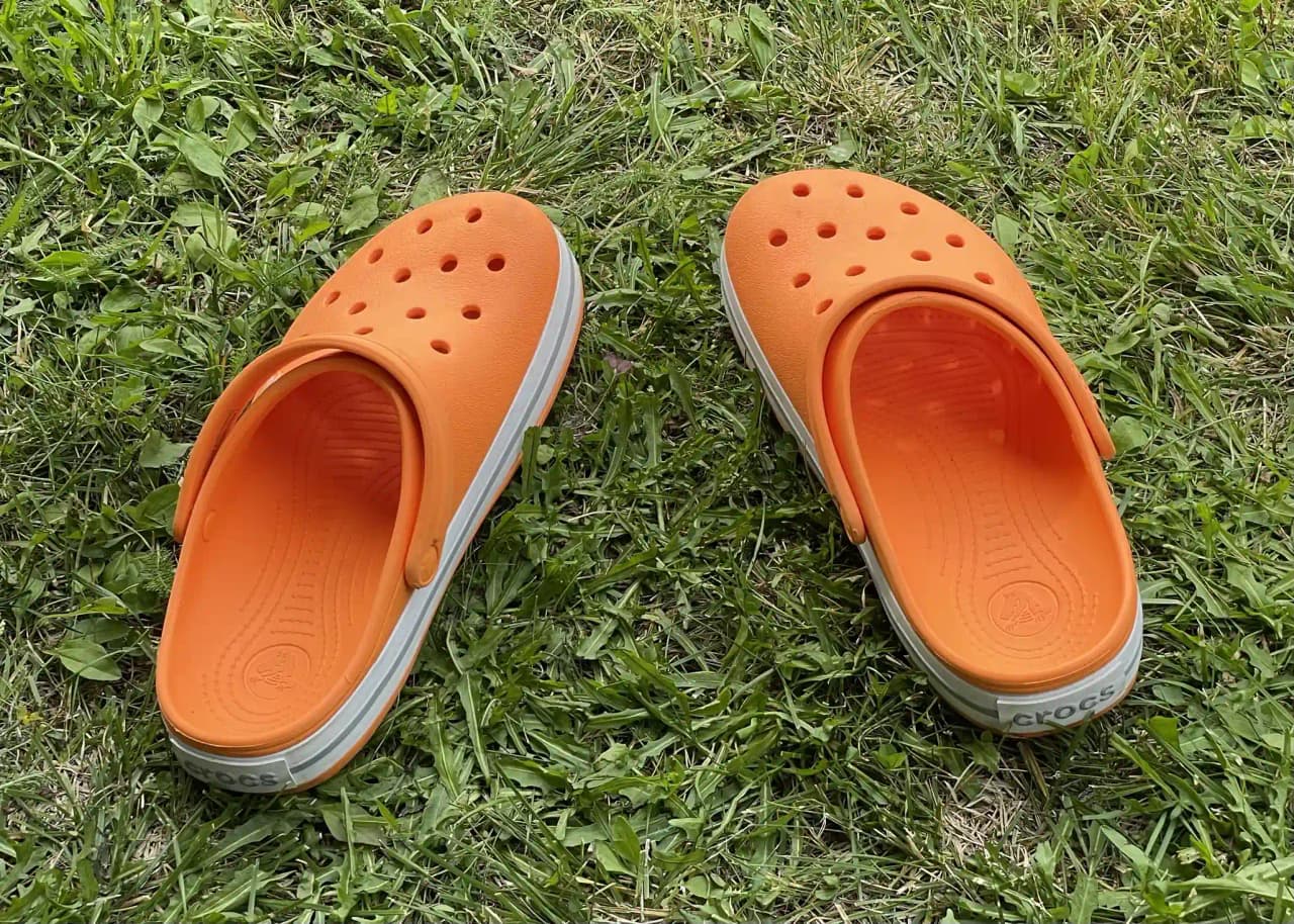 En närbild av en persons fot i en orange och gul sko, ståendes på marken. Bakgrunden är suddig och ger en känsla av sommar och utomhusmiljö, lämplig för fritidsaktiviteter på Kävsta Camping.
