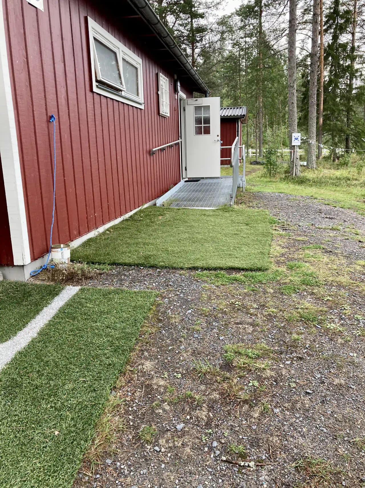 En grönskande trädgård med gräsmatta vid sidan av en grusad uppfart och ett hus i bakgrunden, vid Vallens Turism & Fritid.
