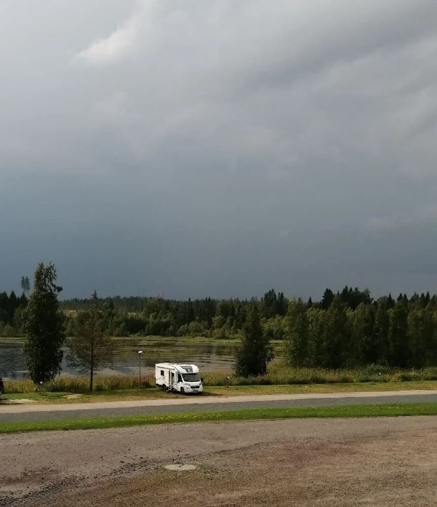 En husvagn och en lastbil parkerade på asfalt under molnig himmel på Gammeltomtens campingplats.