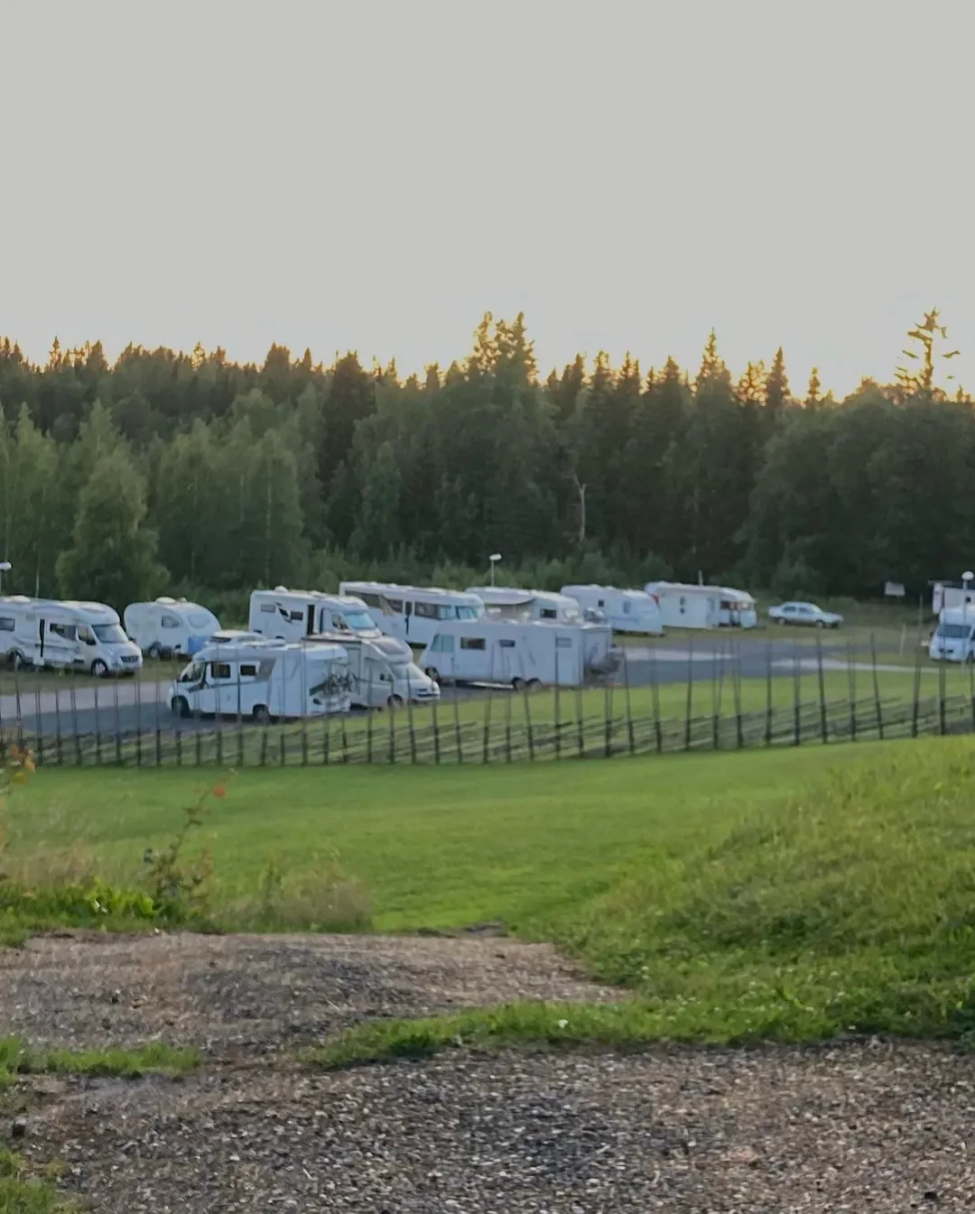 En husvagn och campingfordon parkerade på Gammeltomtens camping, omgivna av grönska och en rymlig parkering.