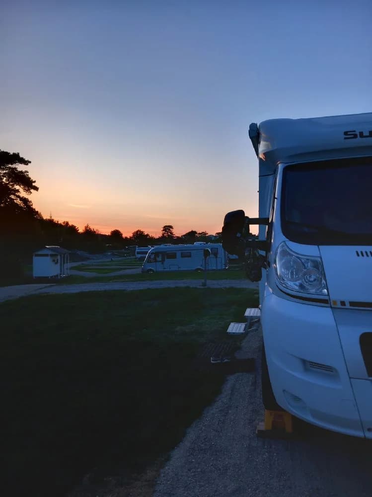 En husbil står parkerad vid Fjällbacka camping under en vacker solnedgång som färgar himlen i varma toner, vilket skapar en lugn och avkopplande atmosfär i skymningen.