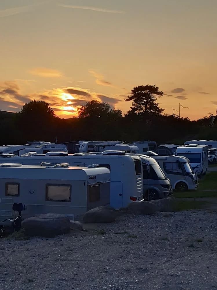 En campingplats vid Fjällbacka i skymningen, med husbilar parkerade under en vacker solnedgång som färgar himlen i röda och orange toner.