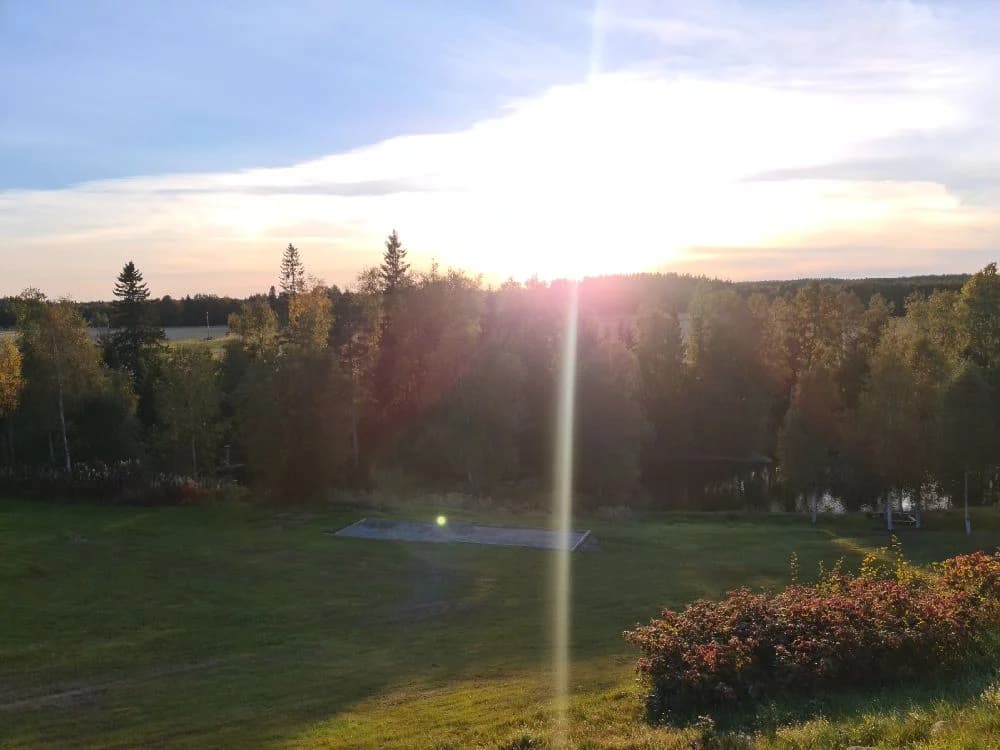 Bild av Lufta Camping & Restaurang. Soluppgång över ett somrigt landskap med vidsträckt himmel, där solen strålar skapar en varm och inbjudande atmosfär mellan horisonten och den öppna naturen.