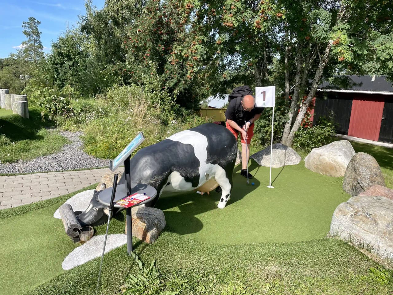 Bild av Lufta camping & restaurang där en grön och välskött gräsmatta syns i förgrunden. I bakgrunden finns utrustning och element som påminner om en golfbana, vilket ger platsen en känsla av stil och rekreation. Vegetation omger området, vilket förstärker den natursköna miljön på campingen.