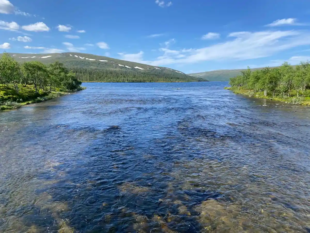 En naturskön vy över en vattensamling i en vildmarksomgivning, omgiven av högländer och banker.