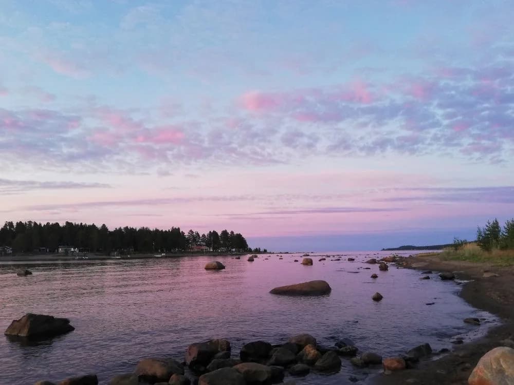 En vacker utsikt över Bovikens havsbad i kvällsljus med molnig himmel och horisonten i bakgrunden, där klippor i vattnet skapar en rofylld stämning.