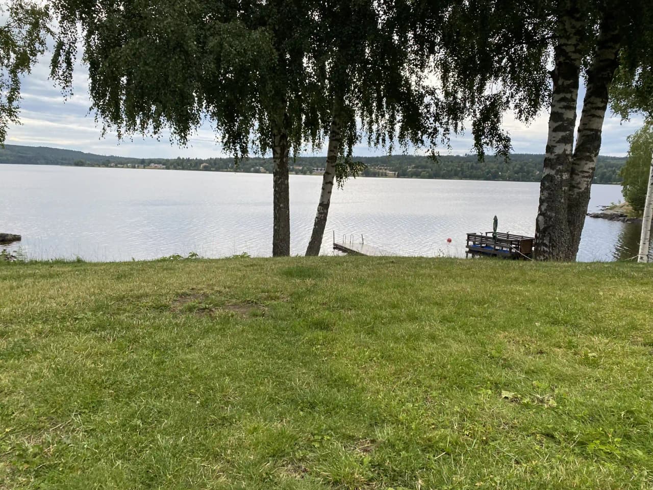 En grön campingplats vid ett lugnt sjölandskap med gräsområden och en välskött park.