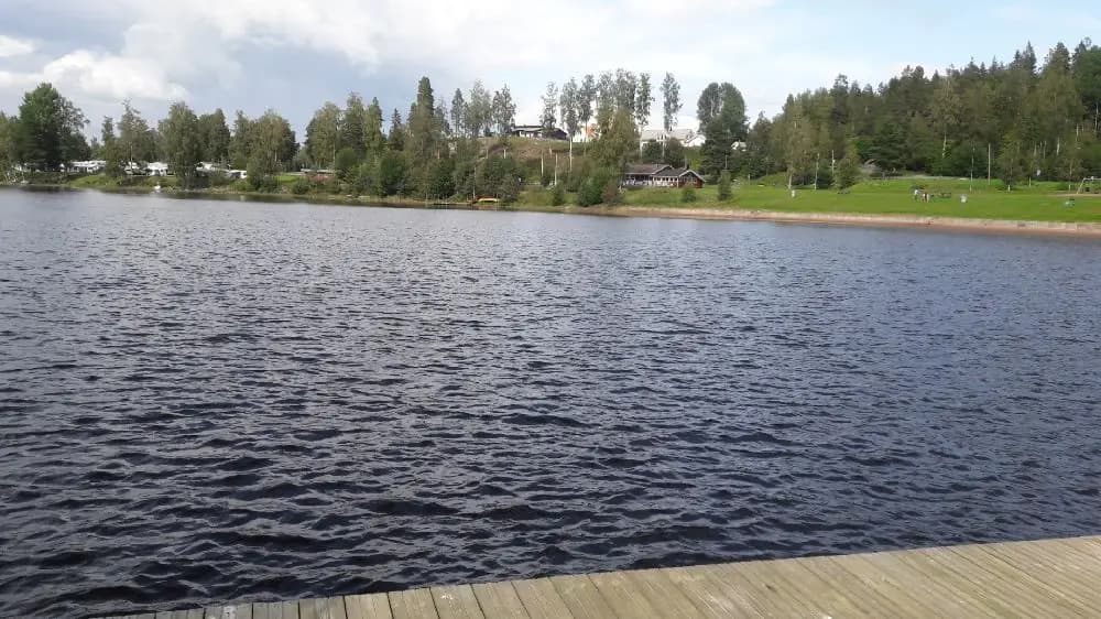 Bild av Säter camping vid en sjö med lugnt vatten där träd och himmel speglas i ytan.